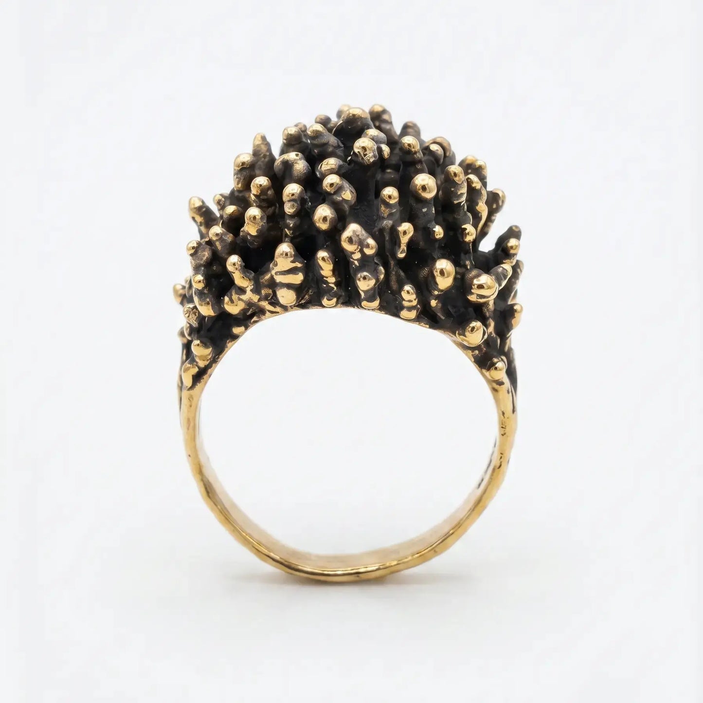 Dettaglio macro della parte superiore di un anello di design in bronzo, texture complessa a noduli dorati su base scura ossidata, gioielleria artistica contemporanea.