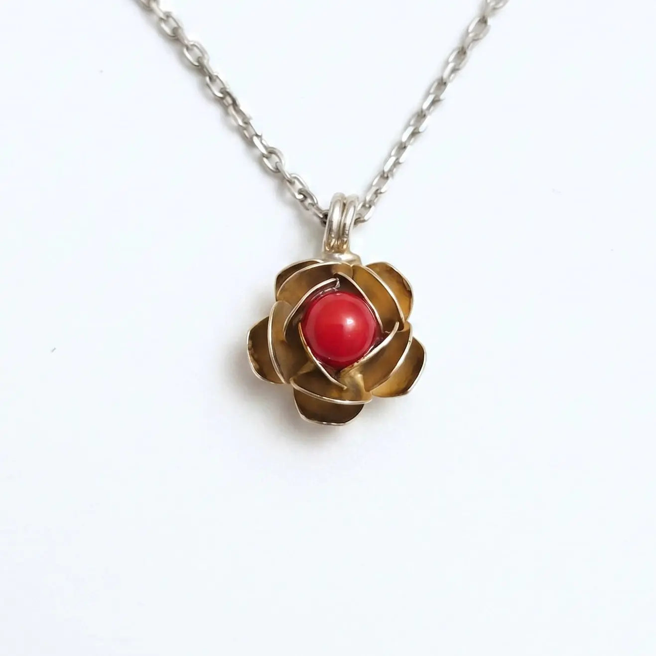 Collana d'argento con ciondolo a forma di rosa in oro e cabochon di corallo rosso centrale, fotografata su sfondo bianco per e-commerce