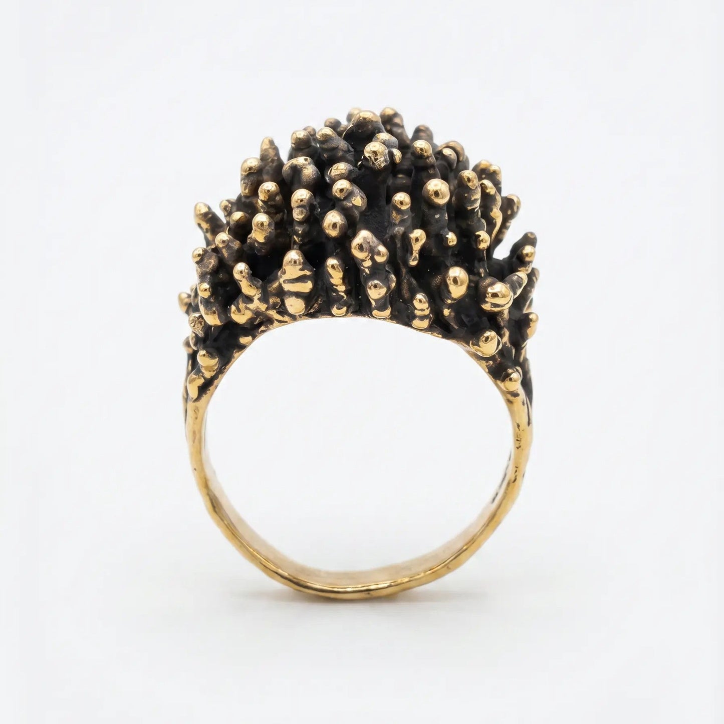 Dettaglio macro della parte superiore di un anello di design in bronzo, texture complessa a noduli dorati su base scura ossidata, gioielleria artistica contemporanea.