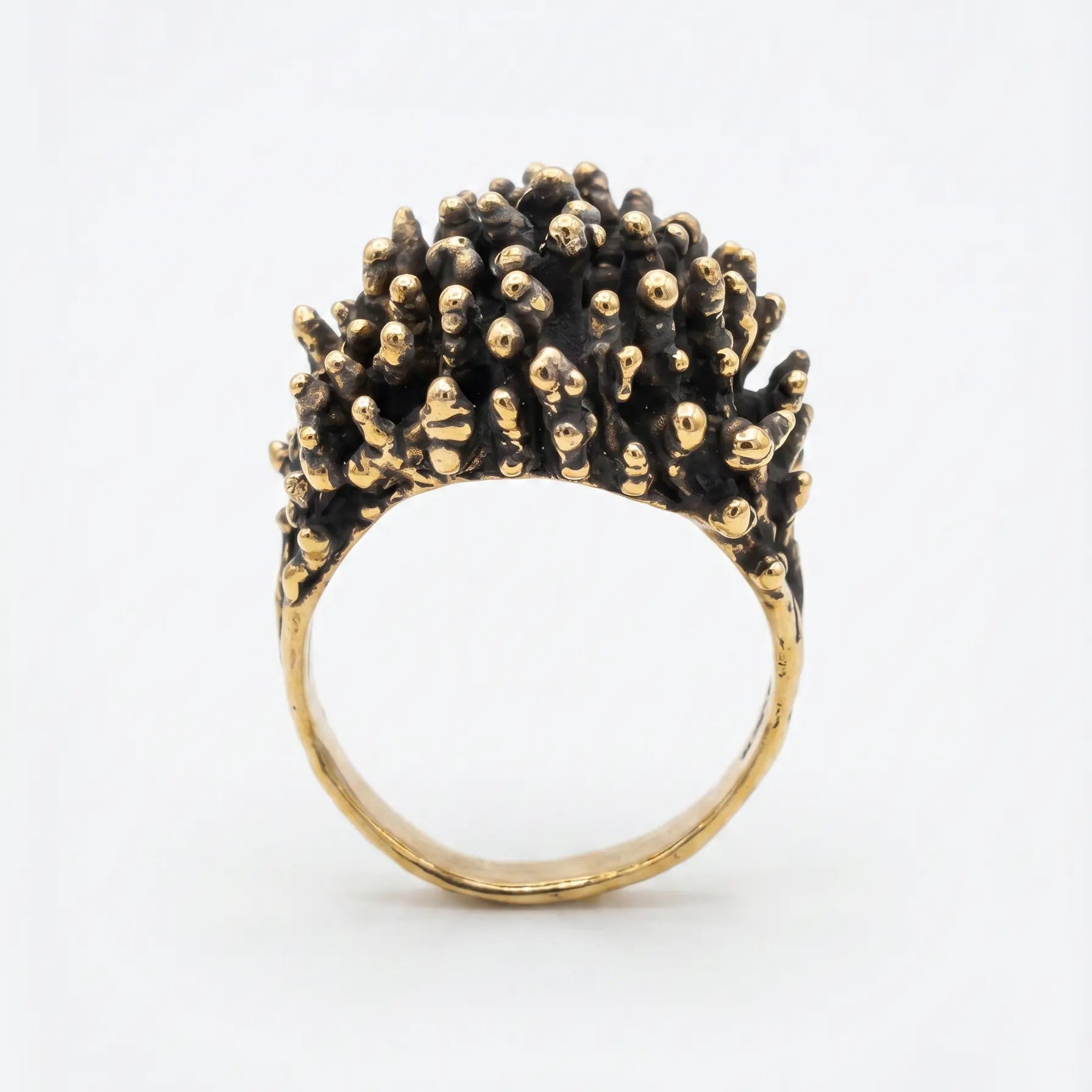 Dettaglio macro della parte superiore di un anello di design in bronzo, texture complessa a noduli dorati su base scura ossidata, gioielleria artistica contemporanea.