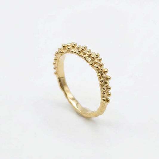 Anello dorato con palline puntinate stile granulazione, design organico e finitura lucida su sfondo bianco assonometria