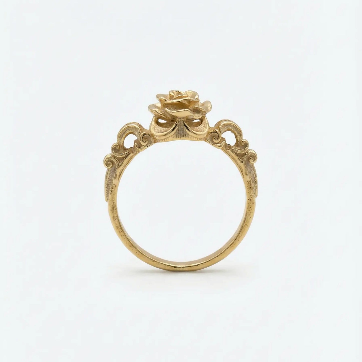 Dettaglio laterale di un anello bronzo dorato con decorazioni barocche a traforo e castone a forma di bocciolo di rosa, design artigianale d'ispirazione antica