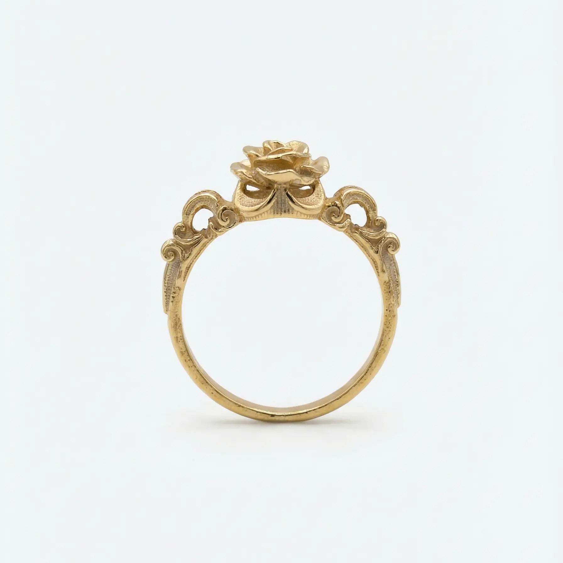 Dettaglio laterale di un anello bronzo dorato con decorazioni barocche a traforo e castone a forma di bocciolo di rosa, design artigianale d'ispirazione antica