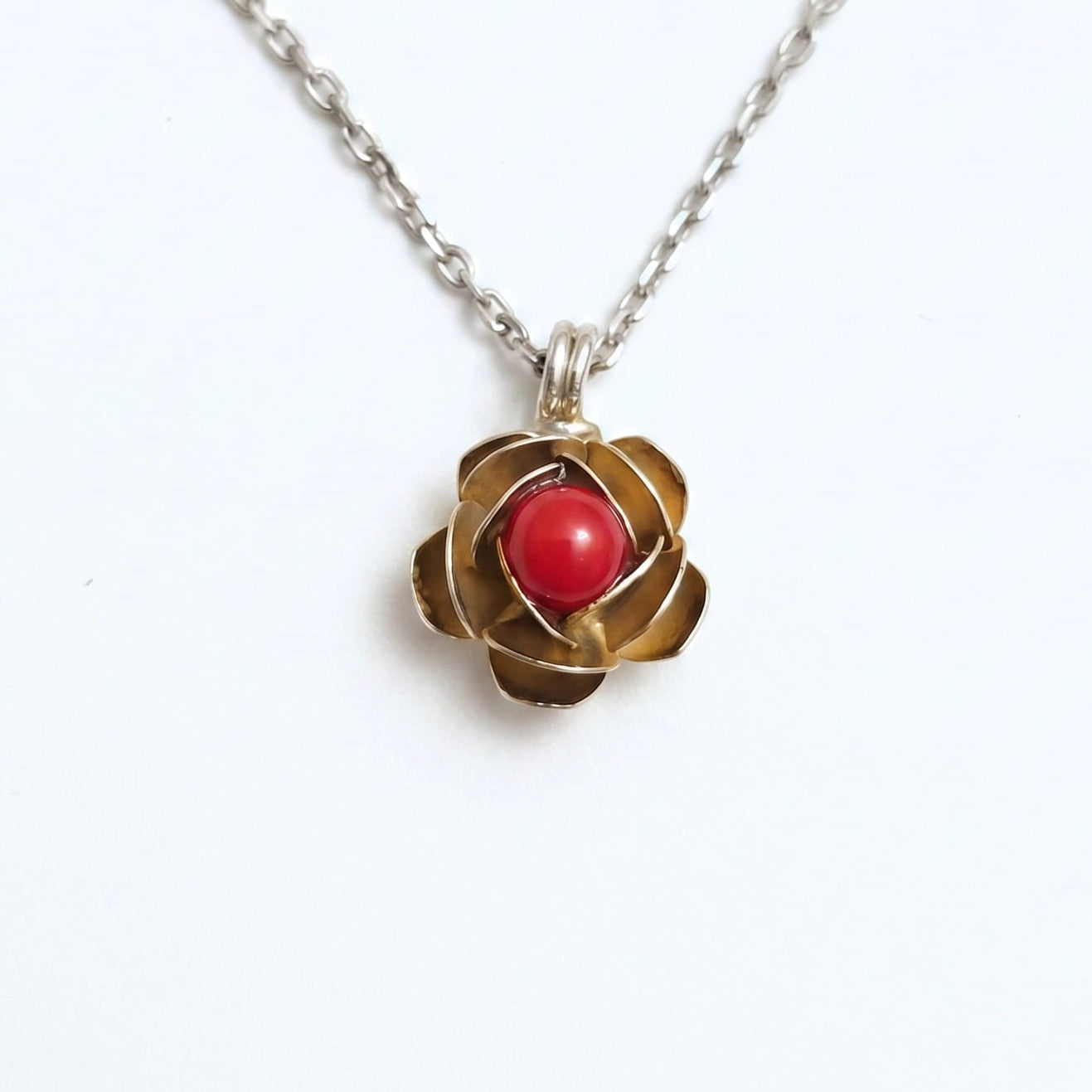 Collana d'argento con ciondolo a forma di rosa in oro e cabochon di corallo rosso centrale, fotografata su sfondo bianco per e-commerce