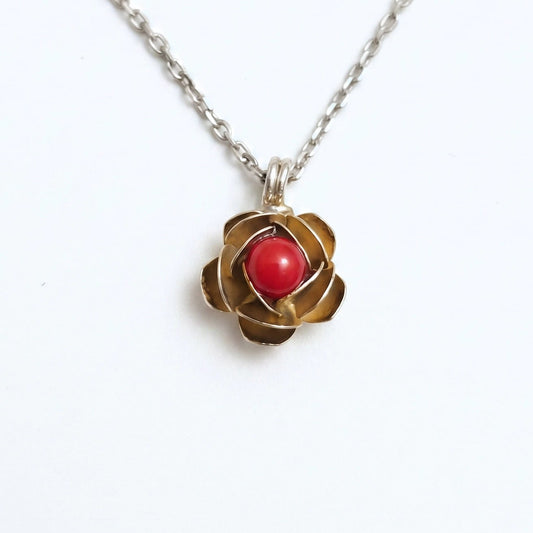 Collana d'argento con ciondolo a forma di rosa in oro e cabochon di corallo rosso centrale, fotografata su sfondo bianco per e-commerce